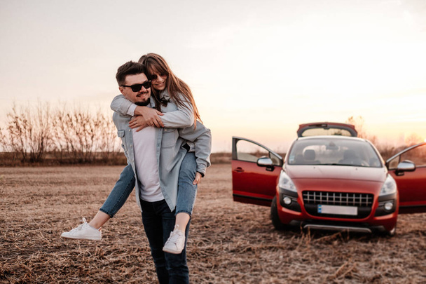 Fiatal boldog pár öltözött Alike fehér ing és farmer Élvezi Road Trip az új autó, gyönyörű naplemente a pályán, nyaralás és utazási koncepció - Fotó, kép