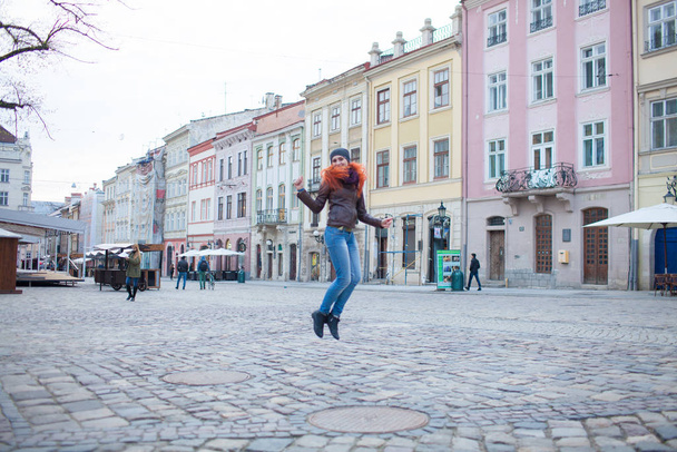町の広場にある赤い髪の少女は、古い建物の背景を楽しんでいます - 写真・画像