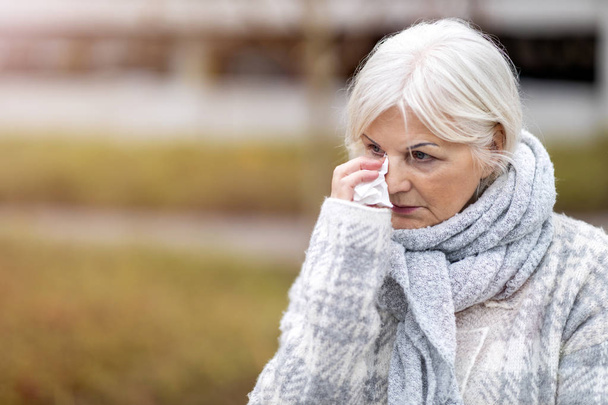 Плачуча стара жінка витирає очі тканиною
 - Фото, зображення