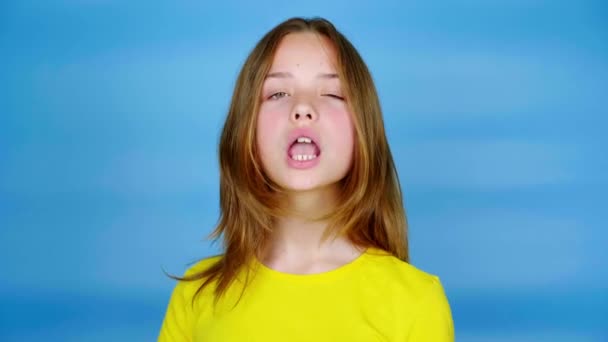 Tiener meisje in een geel t-shirt kijkt naar de camera, knikt met haar hoofd en zegt ja. Blauwe achtergrond met kopieerruimte. Tiener emoties. 4k-beelden - Video
