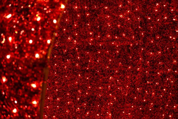ティンセル、点滅するライトやガーランドと赤いクリスマスのお祝いの装飾的な背景。赤と黄色の色で新年の照明装飾。クリスマスストリングライト電球によって照らされた壁. - 写真・画像