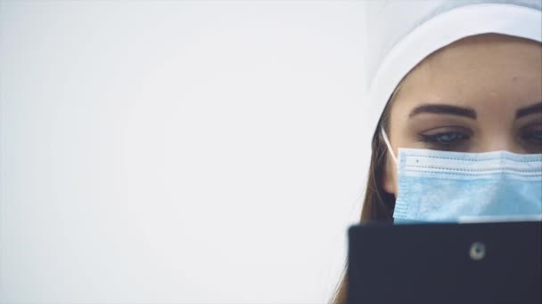 Half-side face of concentrated female intern standing, holding clipboard, checking data, winking her eyes. - Video, Çekim