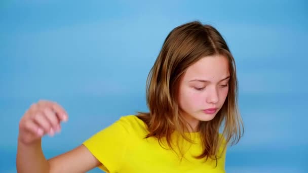 Nastolatka w żółtej koszulce macha i krzyczy, Grimaces. Niebieskie tło z miejscem do kopiowania. Nastoletnie emocje. Materiał 4k - Materiał filmowy, wideo