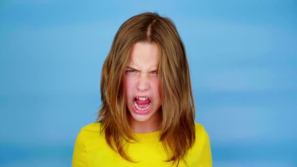Sarı tişörtlü genç kız çığlık atıyor ve gülümsüyor. Kopyalama alanı olan mavi arkaplan. Gençlik duyguları. 4k görüntü - Video, Çekim