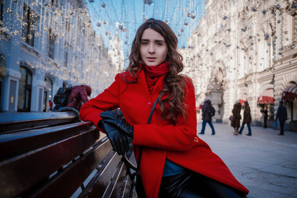 Πορτρέτο μιας νεαρής μελαχρινής γυναίκας με κόκκινο παλτό σε μια κόκκινη πλατεία στο κέντρο της Μόσχας - Φωτογραφία, εικόνα