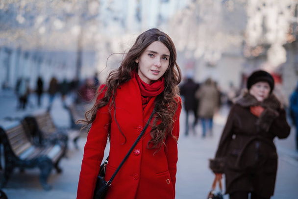 Portrait of a young brunette woman in a red coat on a red square in the center of Moscow - Photo, Image