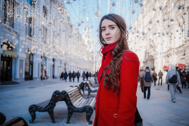 Portrait of a young brunette woman in a red coat on a red square in the center of Moscow - Photo, Image