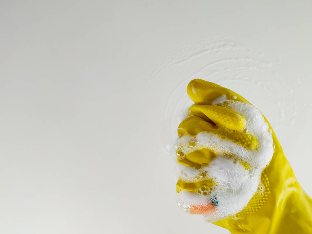 Closeup of a hand squeezing the detergent foam in a yellow rubber cleaning glove while doing the house chores and cleansing - Valokuva, kuva