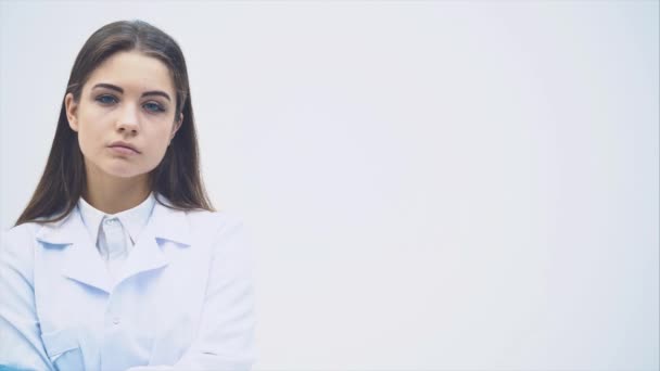 Young female intern standing in medical uniform, looking seriously at the camera, posing, her hands crossed. - Filmati, video