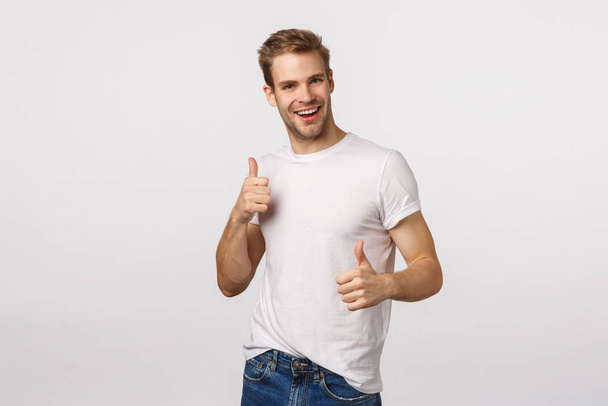 Joyful, charismatic blond bearded guy in white t-shirt, showing thumbs-up and dancing from satisfaction, delight, hear interesting idea, accept plan, agree with friend, give approval, like gesture - Photo, Image