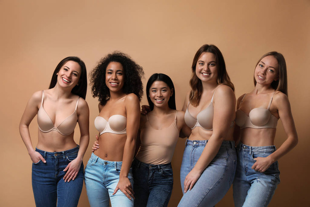 Group of women with different body types in jeans and underwear on beige background - Фото, изображение