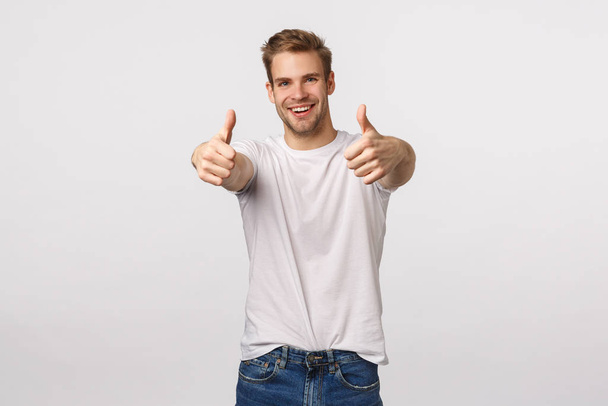 Optimistic and upbeat good-looking blond caucasian guy with bristle, extend hands with thumbs-up to praise friend, congratulate with win, good effort, think product excellent, give approval - Foto, immagini