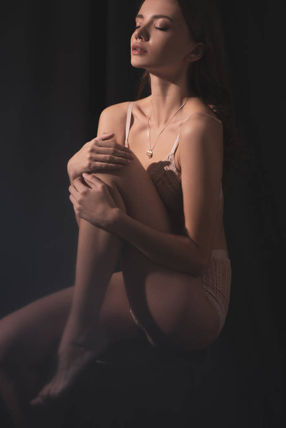 sensual jovem mulher em lingerie posando enquanto sentado com os olhos fechados no fundo preto
 - Foto, Imagem
