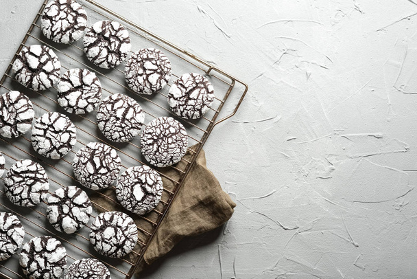 Chocolate crinkle cookies with powdered sugar icing. Cracked chocolate biscuits on an iron lattice on a light background top view copy space - Photo, Image