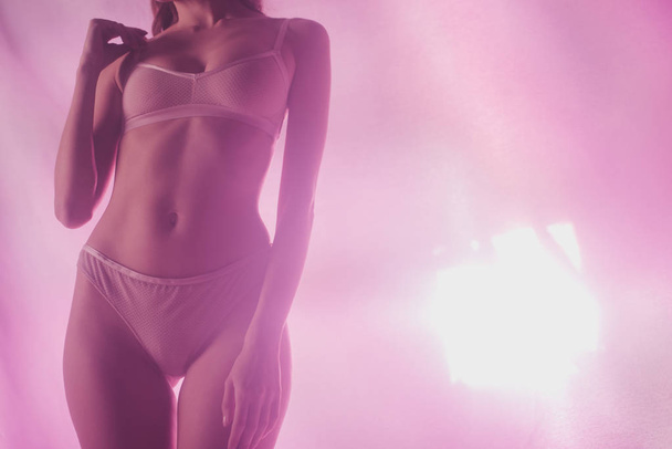 partial view of sexy girl in lingerie holding posing on pink and purple background with lighting - Fotó, kép