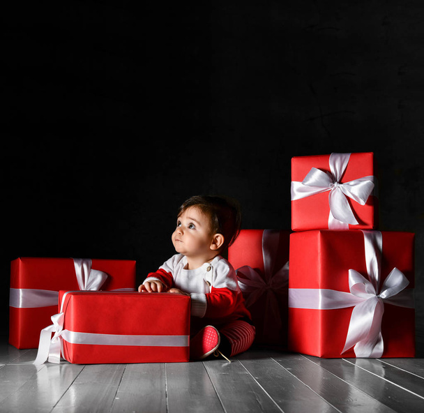 Little baby babe with santa costume with red boxes on a dark background - Фото, изображение