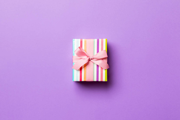 wrapped Christmas or other holiday handmade present in paper with pink ribbon on purple background. Present box, decoration of gift on colored table, top view with copy space - 写真・画像