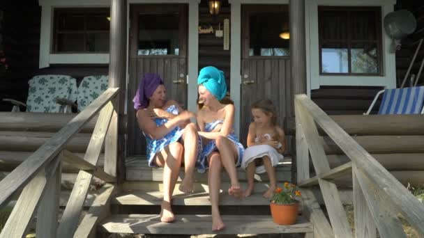 Drie vrouwelijke saunaliefhebbers genieten van frisse lucht op de veranda van een traditionele Finse sauna - Video