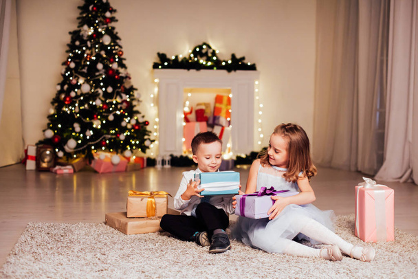 el niño y la muchacha abren los regalos de Navidad el árbol de Navidad la fiesta de Nochebuena familiar
 - Foto, imagen