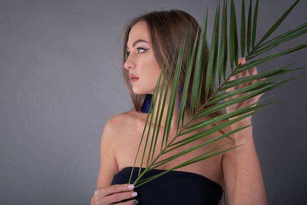 Portrait of young and beautiful woman with perfect smooth skin in tropical leaves. Concept of natural cosmetics and skincare. young beautiful woman with a palm leaf, clean skin - Foto, Bild