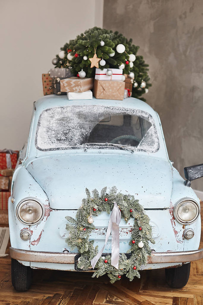 Christmas decorated classic car. A vintage car decorated for New year holidays loaded with festive gifts. Christmas retro car decorated loaded with Christmas tree and presents - Фото, изображение