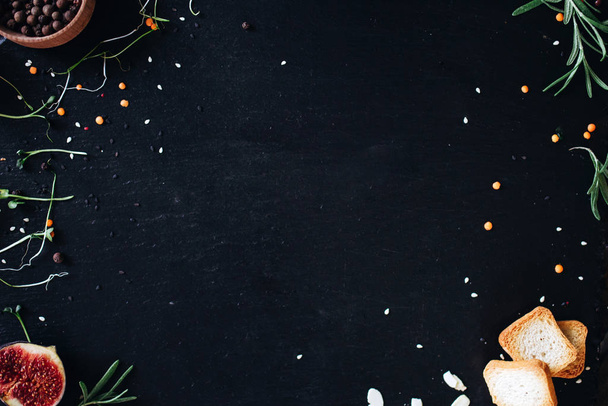Μαύρη σανίδα με κόκκους πιπεριού, δενδρολίβανο, σύκα και φρυγανιές. - Φωτογραφία, εικόνα