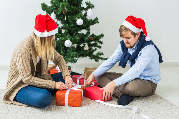 Holidays, relationship and festive concept - Couple opening present together by Christmas tree - Foto, Imagen