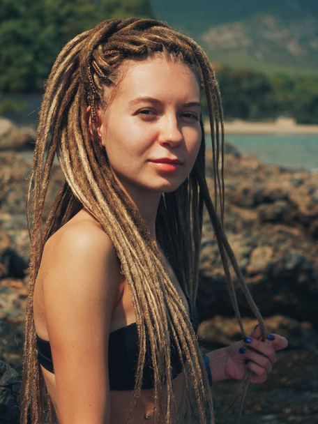 Young woman with dreadlocks sitting on the rocks  - Foto, afbeelding