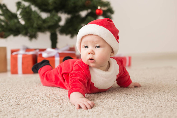 Cute baby girl wearing santa claus suit crawling on floor over Christmas tree. Holiday season. - Fotoğraf, Görsel