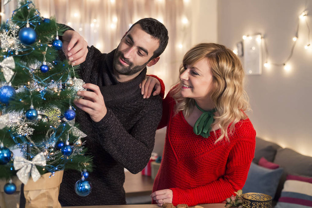 Friends enjoying decorating Christmas tree in living room. Holidays preparation. - Photo, Image