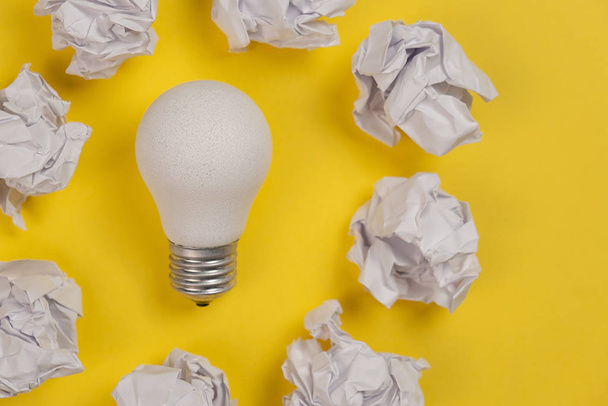 Creativity inspiration, great business idea concept with white light bulb and paper crumpled ball on yellow background. Flat lay, top view, copy space - Photo, Image