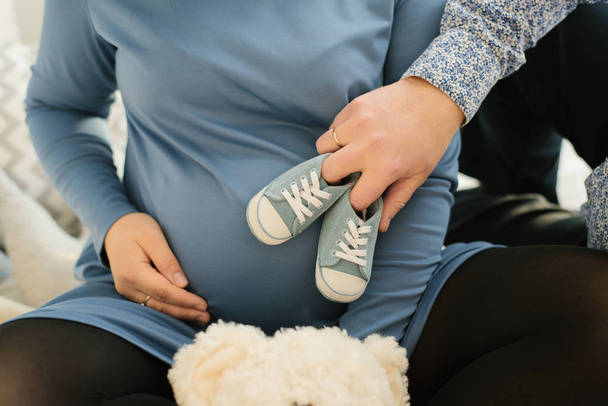 Un futuro padre sostiene zapatillas azules de un bebé nonato en el estómago de su esposa embarazada, de cerca
 - Foto, imagen