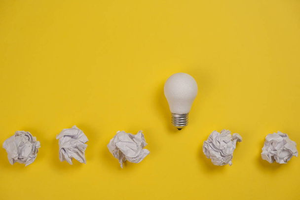 new idea concept with crumpled office paper and white light bulb on yellow background. Creative solution during brainstorming session concept. Flat lay, top view, copy space - Photo, Image