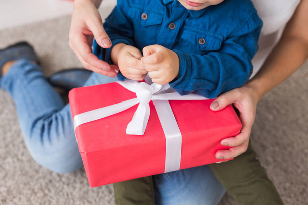 Χριστούγεννα, μόνος γονέας και έννοια των διακοπών - Κοντινό πλάνο του χαριτωμένο μικρό αγόρι κρατώντας χριστουγεννιάτικο δώρο για τη μητέρα του στο σπίτι. - Φωτογραφία, εικόνα