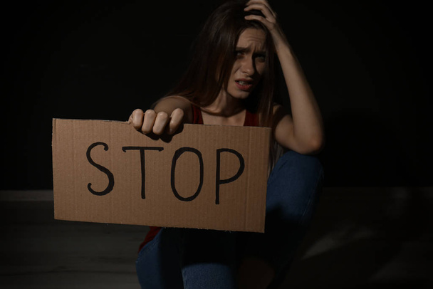 Crying young woman with sign STOP on black background. Domestic  - Фото, изображение