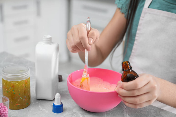 Little girl mixing ingredients with silicone spatula at table indoors, closeup. DIY slime toy - Foto, imagen