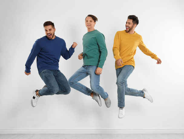 Group of young men in stylish jeans jumping near white wall - Fotografie, Obrázek
