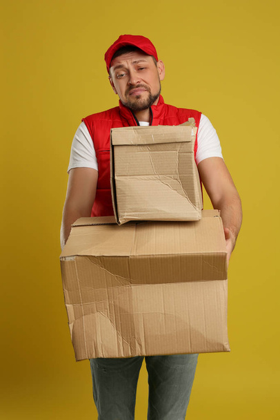 Emotional courier with damaged cardboard boxes on yellow backgro - Zdjęcie, obraz