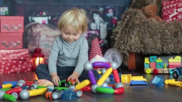 Sweet blonde toddler boy, playing with plastic construction, making different shapes, christmas decoration around him - Πλάνα, βίντεο