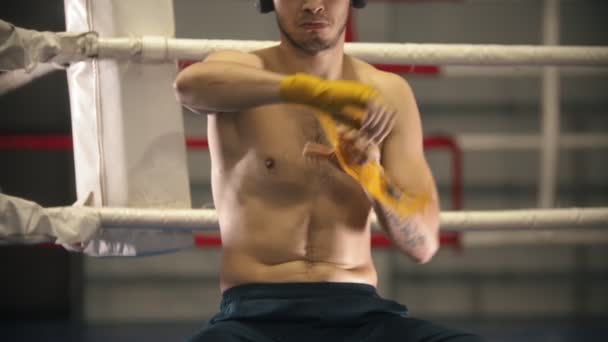 Trening bokserski - człowiek siedzący na rogu ringu i bandażujący ręce - Materiał filmowy, wideo