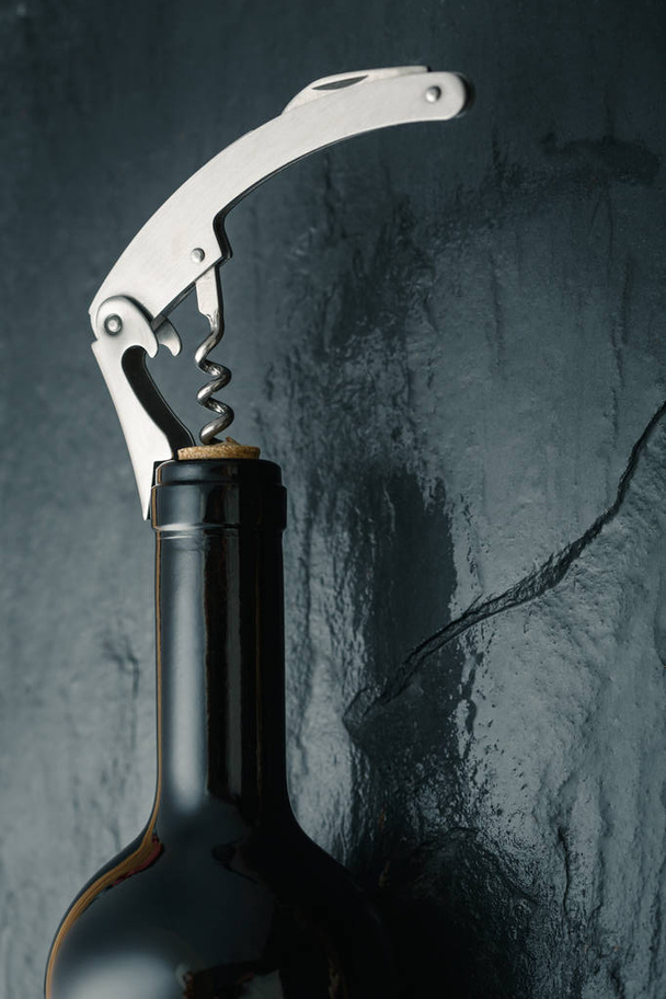 Stainless  wine corkscrew in a cork of wine bottle neck on a bla - Photo, image