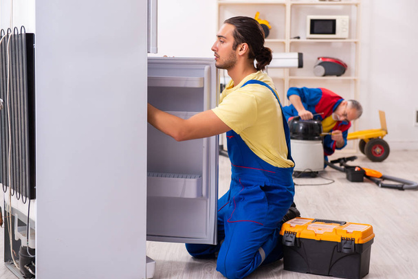 Два підрядники ремонтують холодильник на майстерні
 - Фото, зображення