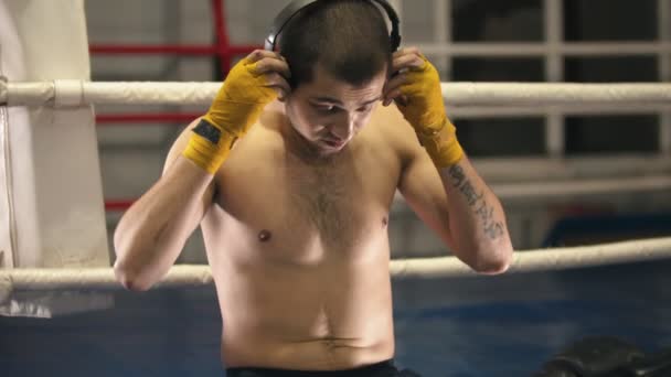 Boxtraining - ein Mann sitzt auf dem Ring - setzt Kopfhörer und Handschuhe auf - Filmmaterial, Video