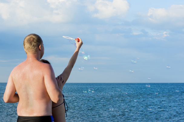 Mies ja tyttö aloittavat saippuakuplat merellä. Näkymä edestakaisin
 - Valokuva, kuva