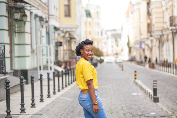 Lifestyle street girl. African American girl in a yellow T-shirt and blue jeans - Foto, afbeelding