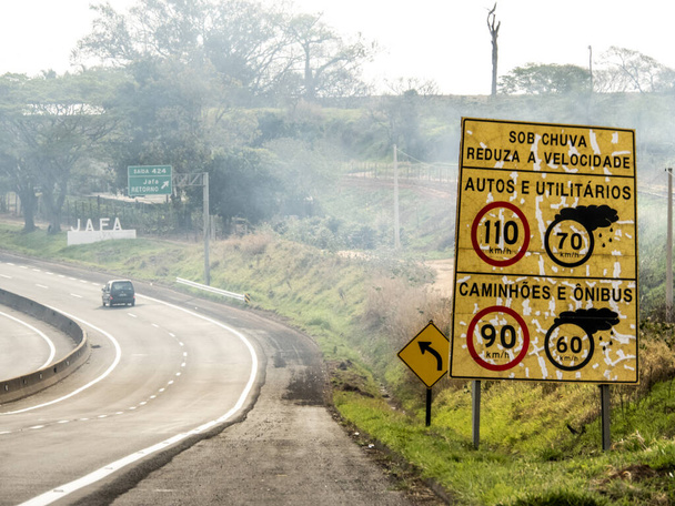 Signpost indicating speed limit on dry and wet roads on Comandante Joao Ribeiro de Barros Highway, SP 294, near the entrance of Jafa district, in Garca municipality - Photo, Image