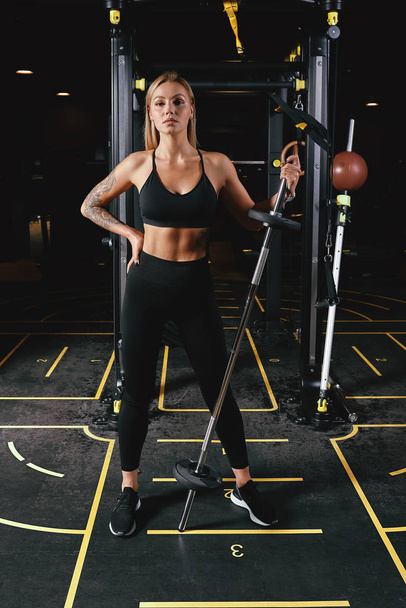 Front view of confident young blonde woman doing weight lifting workout Attractive young woman looking forward Strong trained body shape arms chest legs. - Фото, изображение