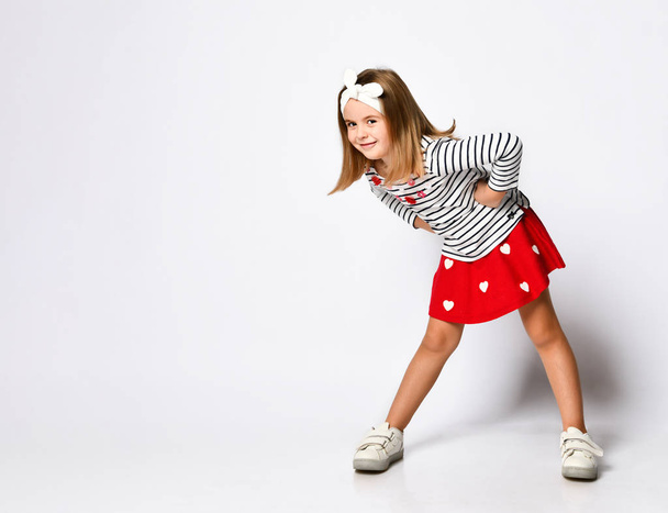 Happy child little girl in a red skirt and a striped T-shirt, with a perky hairband - has fun on a light background - Foto, afbeelding