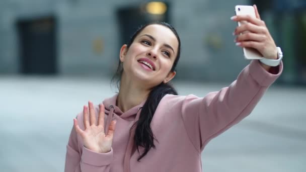 Una mujer sonriente saludando de la mano a la cámara. Chica feliz usando el teléfono móvil
 - Metraje, vídeo