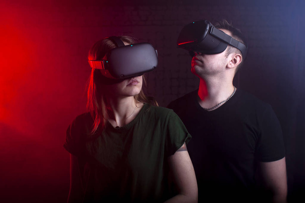 τύπος και κορίτσι σε ασύρματα γυαλιά της εικονικής πραγματικότητας σε ένα σκοτεινό φόντο νέον, ένα ζευγάρι μαζί στον εικονικό κόσμο - Φωτογραφία, εικόνα